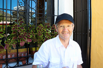 portrait of a happy senior man on holiday sitting outside  in the sun smiling, with plants in a window box behind him