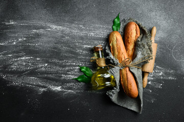 Fresh crispy baguette, a jar of oil and a rolling pin on a dark background. Free space for text.