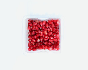 Plastic punnet full of lush red pomegranate seeds against plain white background