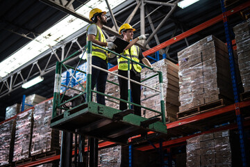 Caucasian warehouse workers with clipboard standing on scissor lift near shelves with clipboard...