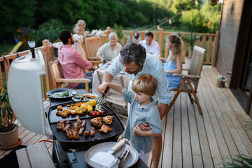 Father with little son grilling outside during family summer garden party. - obrazy, fototapety, plakaty