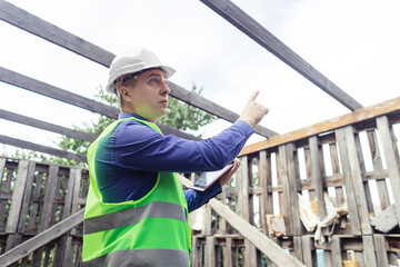 Building inspector. Man in a hard hat and a yellow reflective vest examines damaged structures and inspects the building. Damage assessment. Preparing for the repair or construction of a building