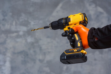 Male worker holds a close-up electric cordless screwdriver in his hands against the background of a construction tool and a concrete wall.