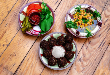 Top view falafel balls, fresh humus and vegetables on a wooden background. Middle east cuisine.