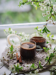 A cup of espresso on a velvet napkin by the window, spring time. Blossoming branches of white cherry