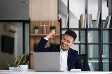 Happy young businessman looking at laptop computer in office, Excited asian man working at his...