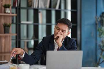 A businessman looks tiredly at a computer monitor and feels hopeless. A young man in a suit works in the office.