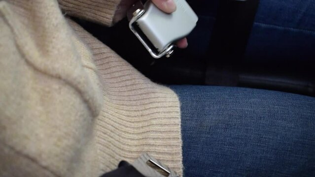 Female passenger undoing and opening seatbelt in commercial airplane after flight. Flight safety measures for turbulence and airline transportation. The woman unbuckles the safety belt.