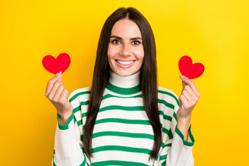 Photo of funny adorable woman wear striped sweater smiling rising tow red hearts isolated yellow color background