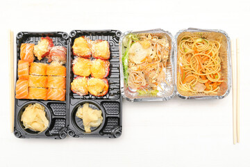 Set of fish sushi rolls with salmon,ginger,wasabi,noodles, salad packed in plastic disposable food container box on white background.Seafood, Food delivery,take out service from restaurant concept