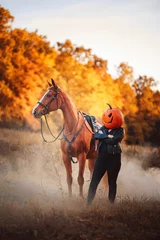Foto op Canvas Vertical shot of a female with pumpkin head standing next to a horse in autumn © Veronika Martinková/Wirestock Creators