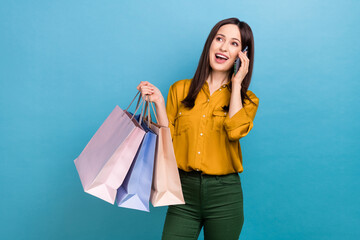 Photo of sweet excited woman wear yellow shirt holding shoppers talking gadget looking empty space...