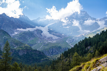 Panorama along the path in the Alta Valsesia Natural Park in summer. Trekking in the mountains. View of the peaks, meadows, trees and woods and sky. Italian Alp. Alagna Valsesia. Piedmont. Alps Italy