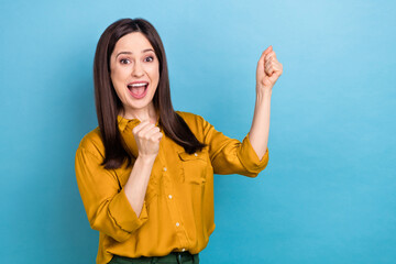 Photo of excited lucky lady dressed yellow shirt rising fists emtpy space isolated blue color...