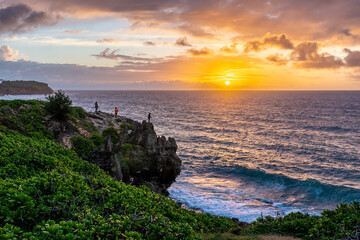 Men, fishermen, standing, fishing, on the edge of a cliff over the ocean, with the sun rising over...