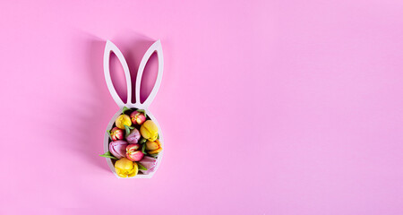Wooden easter bunny statuette with spring tulips on the pink background, easter minimal concept, top view with copy space