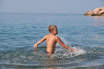 Happy joyful teen boy swim and splash in sea. Sunny summer day, holiday vacation