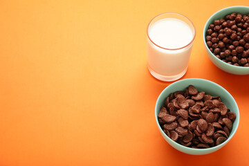 Bowl with cereals and a glass of milk on orange background. Top view