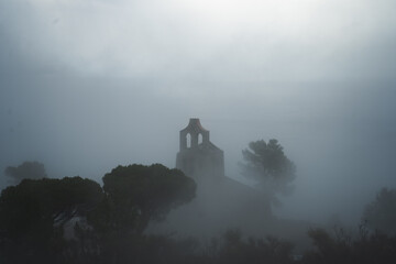 Old church on a mountain hidden in fog with trees around it