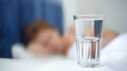 Young woman in the bed in bedroom at home in the morning lying under white blanket and drinking pure fresh water from glass 