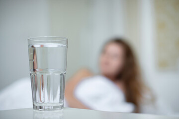 Young woman in the bed in bedroom at home in the morning lying under white blanket and drinking pure fresh water from glass 