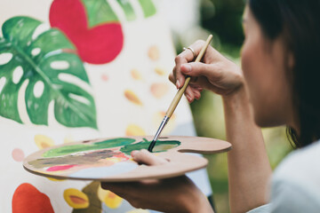 Young asian woman artist painting on canvas..Female artist drawing with inspiration in garden.