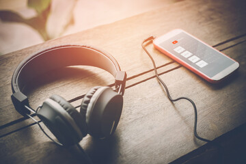 Headphones listening to playlist music media on mobile phones placed on the wood table in sunset light effect background - obrazy, fototapety, plakaty