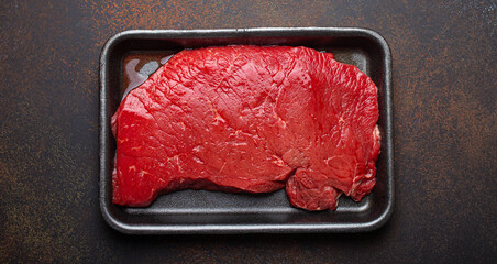 Raw uncooked top round beef steak with blood in black polystyrene tray from supermarket on dark...