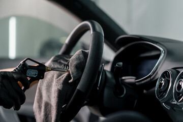 A mechanic in gloves cleans the steering wheel with a microfiber cloth and blows dust with a special tool
