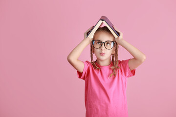Back to school concept. Smiling pretty little school girl in glasses is holding book over head like roof isolated on pink background. Childhood lifestyle concept. Education in school. September 1