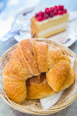 Croissants on wooden basket and Raspberry cake in the background