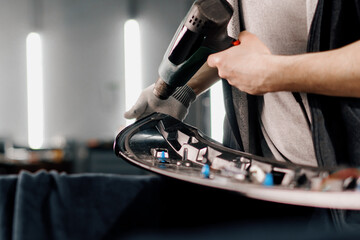 A worker covers a car spoiler with a film in the workshop using a hair dryer and a spatula close-up...