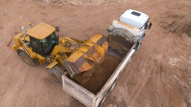 Bucket loader loading soil onto a truck trailer, Top down view
