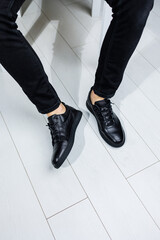 Male legs in black jeans close-up in black leather casual sneakers. Comfortable men's demi-season shoes