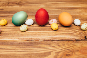 Colored eggs of different sizes on a brown wooden background. Symbol of the Easter holiday. Easter background, top view