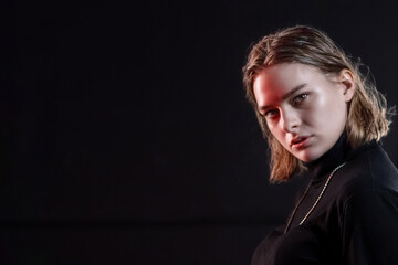 Naklejka premium A slender, beautiful young girl in black clothes poses in a neon red-blue light on a black background.Black on black. Neon