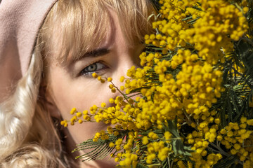 A young woman stands with a bouquet of yellow mimosa and sniffs flowers in the park. The concept of the Spring holiday - March 8, Easter, Women's Day