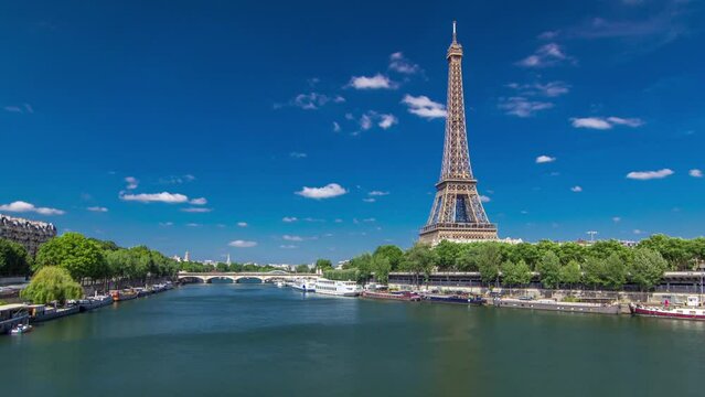The Eiffel tower timelapse hyperlapse from Bir-Hakeim bridge over the river Seine in Paris. Ship and boats on river at sunny summer day with clouds on a blue sky
