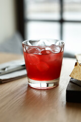 Glass of refreshing red cocktail with ice and soda served on table in a bar