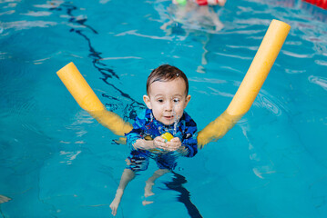 Happy little boy learning to swim with pool noodle