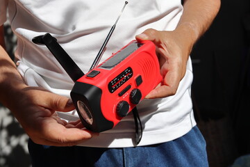 A man holds in his hands a small red portable radio rechargeable with solar panels or manually with...