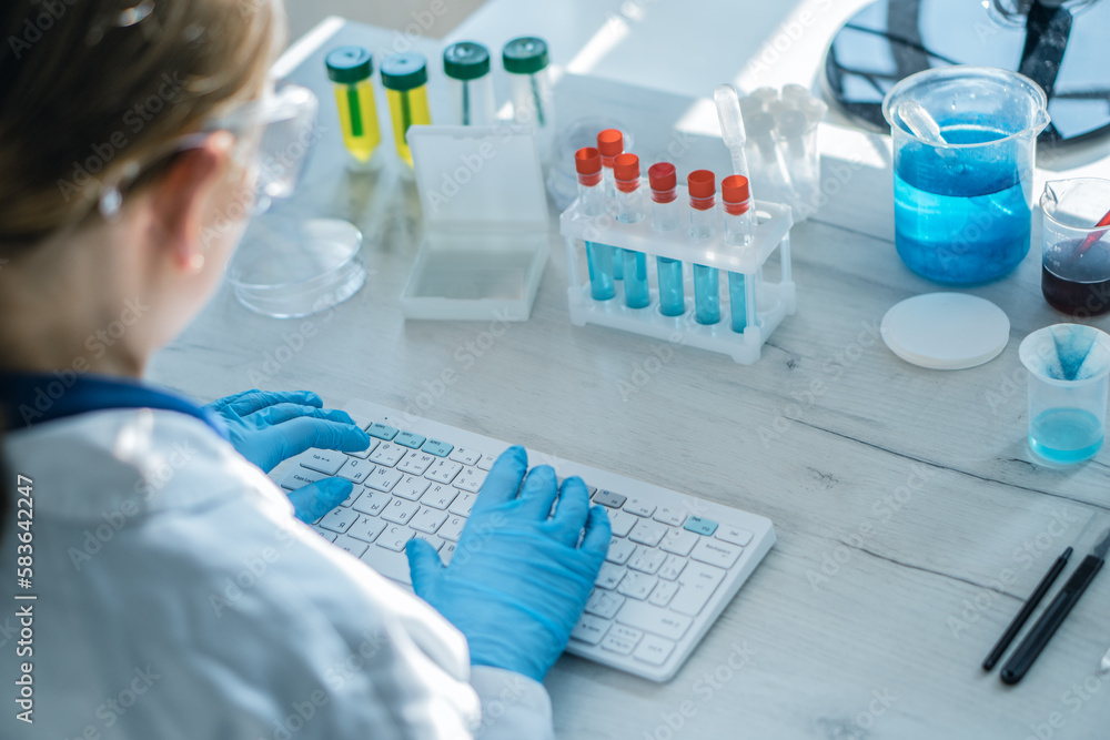 Poster a female researcher sits at a workplace in a laboratory, behind a personal computer monitor. against