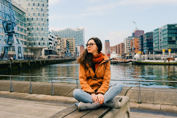 Smiling young woman sitting on sthe bench at Hafencity, Hamburg, Germany
