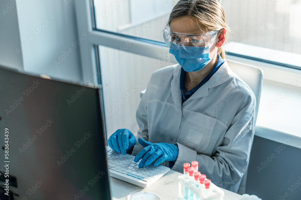 Poster a female researcher sits at a workplace in a laboratory, behind a personal computer monitor. against
