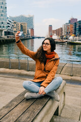 Happy woman taking selfie through smart phone in Hafencity, Hamburg, Germany