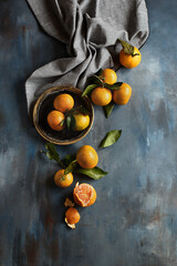Ripe juicy clementines or tangerines with leaves on blue abstract background. Top view, flat lay
