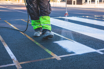 Process of making new road surface markings with a line striping machine, workers improve city infrastructure, demarcation marking of pedestrian crossing with a hot melted paint on asphalt pavement