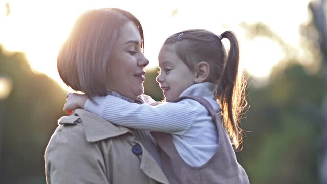 An adorable, sweet little girl hugs her young mother during a walk in a spring park.