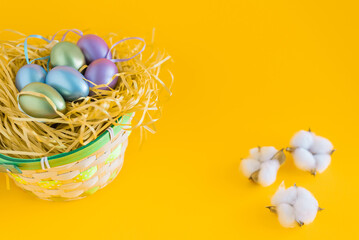 Multicolored Easter eggs in a basket on a bright orange festive background.cotton lies next to the background. Greetings and presents for Easter Day celebrate time.