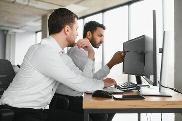 Two successful trader sitting in office and looking at screen, checking cryptocurrency information data on finance market graph, pointing on monitor